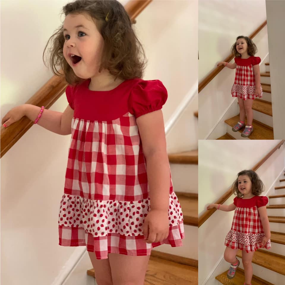 Millie dress pdf sewing pattern by Frocks & Frolics. Empire line bodice and slightly gathered skirt. Puff sleeves with elastication. Patch pockets with piping. Bodice has a cute lace trim. The fabric is white polka dots on a red cotton.