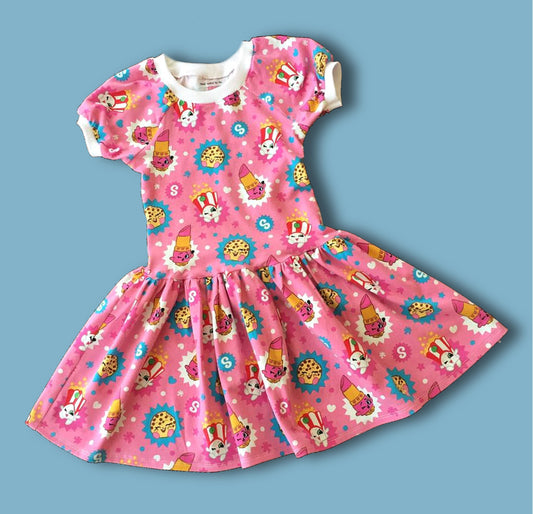 Amelie raglan dress, pdf sewing pattern by Frocks & Frolics. Raglan puff sleeves and ribbed neckband. Low gathered waist. Dress in Jersey with kiddo pink print and white trim.