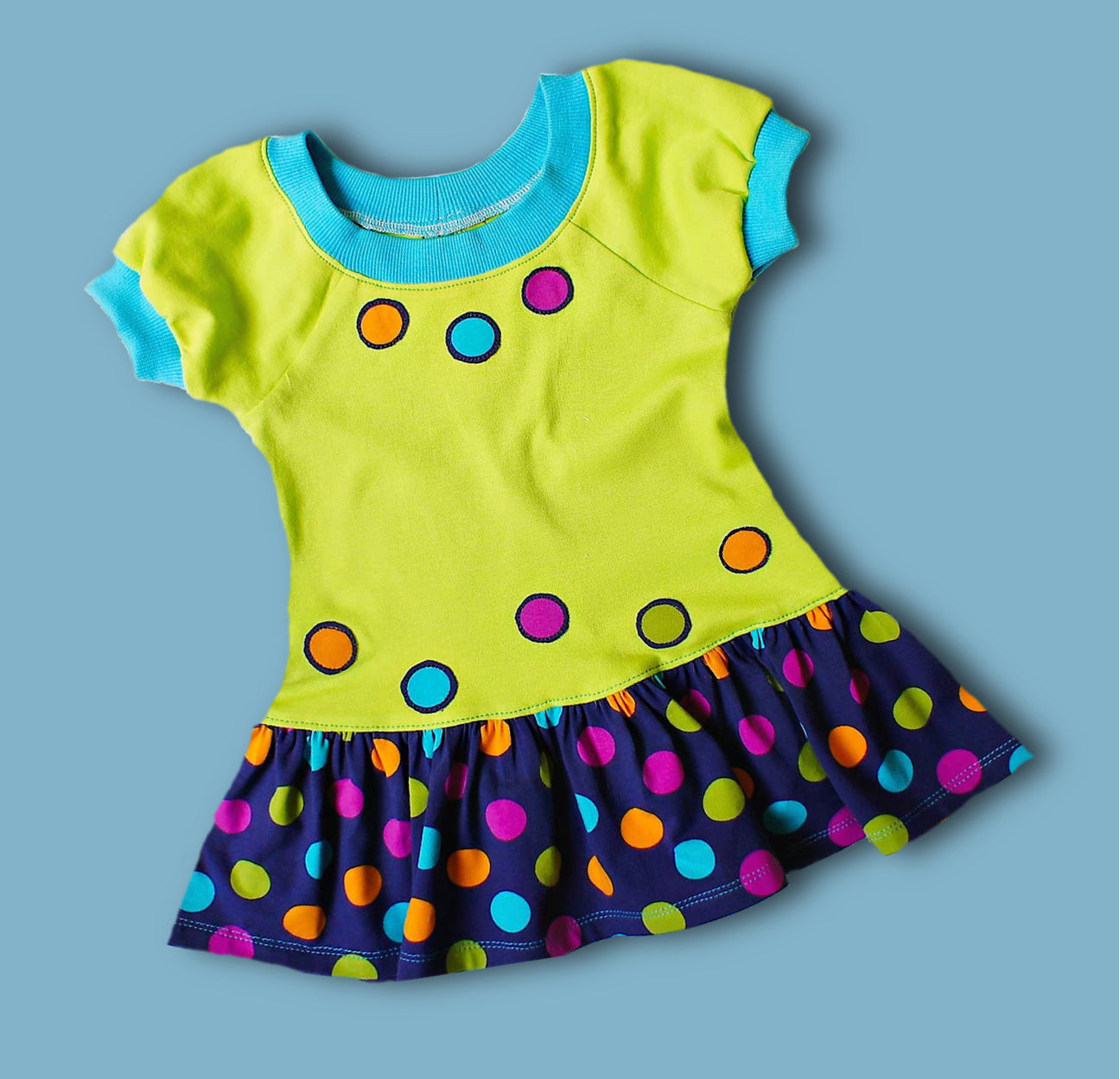 Amelie raglan dress, pdf sewing pattern by Frocks & Frolics. Raglan puff sleeves and ribbed neckband. Low gathered waist. Dress in Jersey with kiddo pink print and white trim.