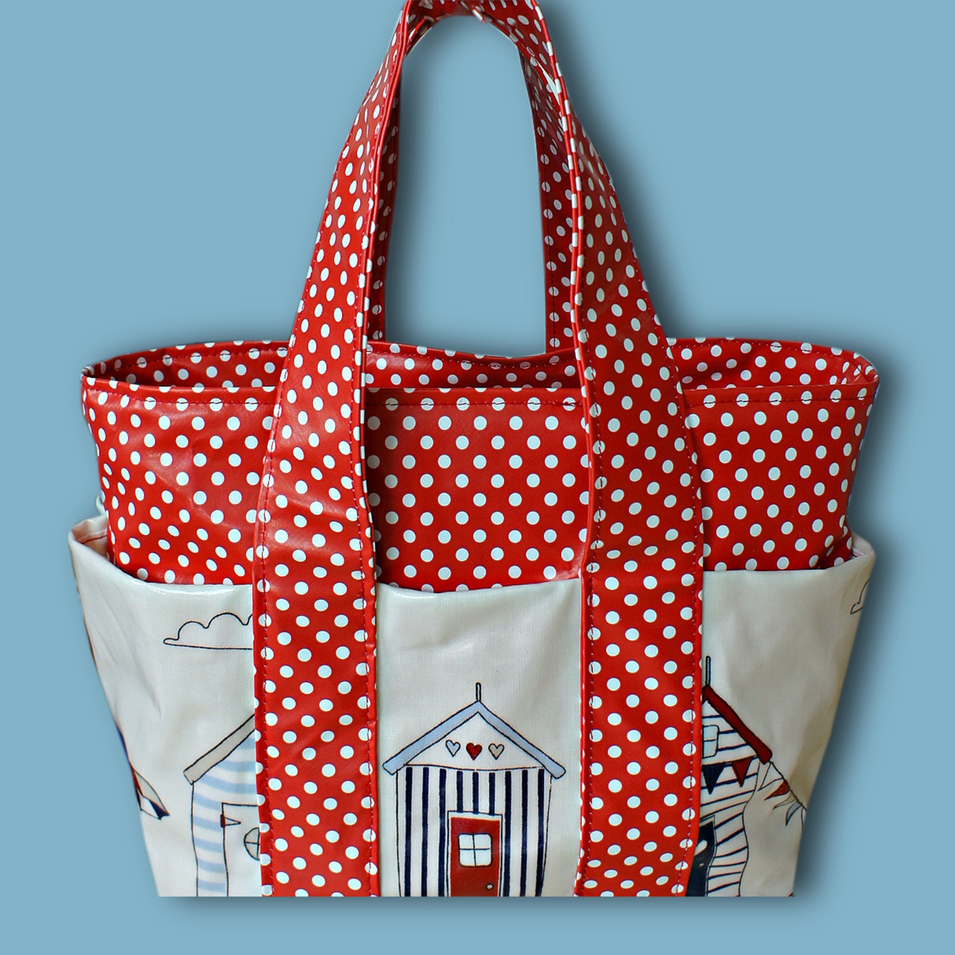 Mini tote bag in red oil cloth with white polkadots. Side view showing the outer pockets. The handles are short and wide. This pdf sewing pattern comes with a video guide.