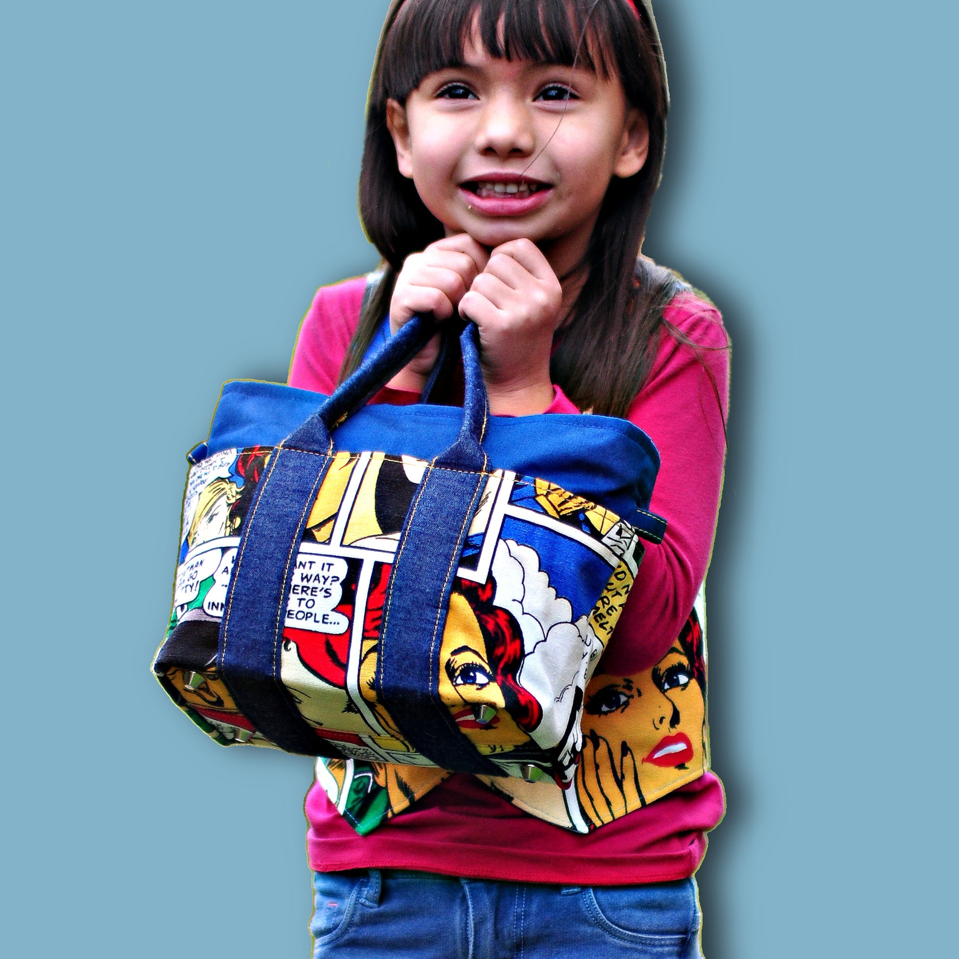Mini tote bag in blue denim with Marvel contrast fabric for this kids bag pattern. Little girl holding the bag.