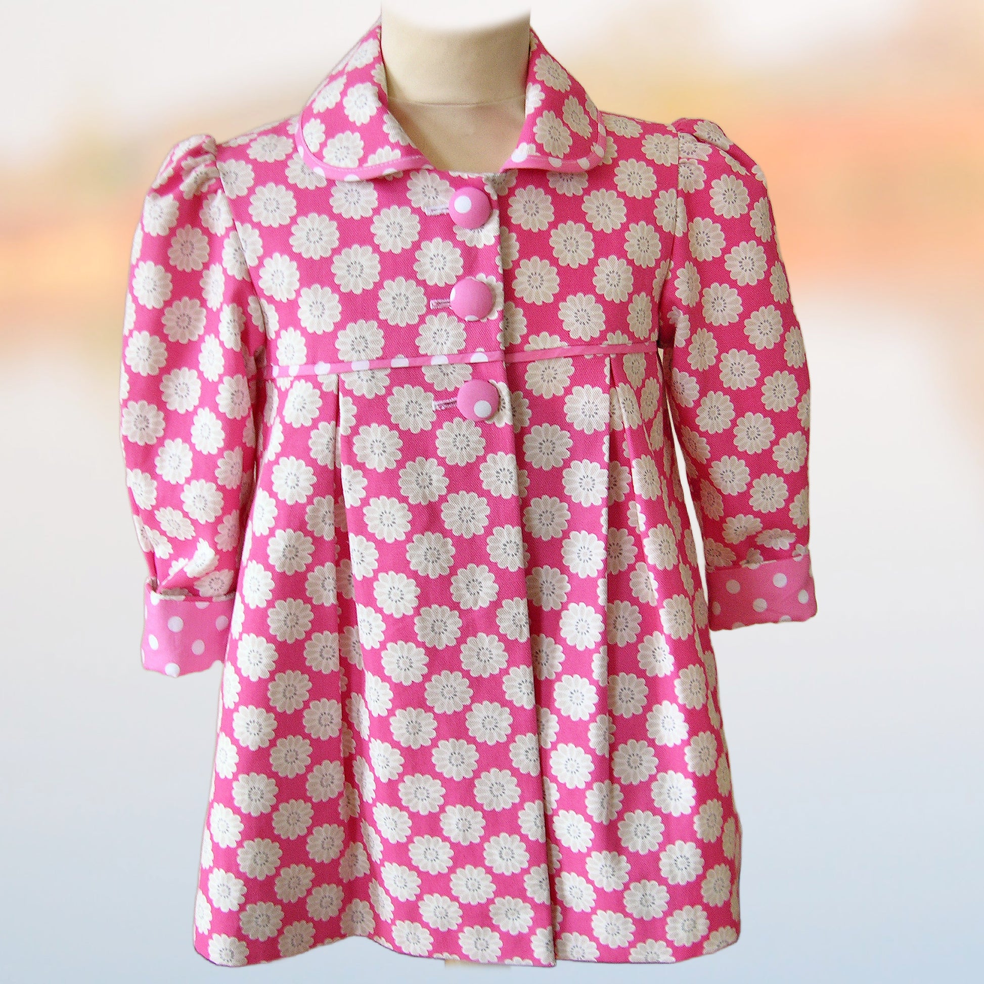 Charlotte girls coat, pdf sewing pattern by Frocks & Frolics. In upholstery cotton with large flower print. Long puff sleeves with cuffs and tabs. Featuring a yoke and rounded collar. Front view. Includes video tutorials.