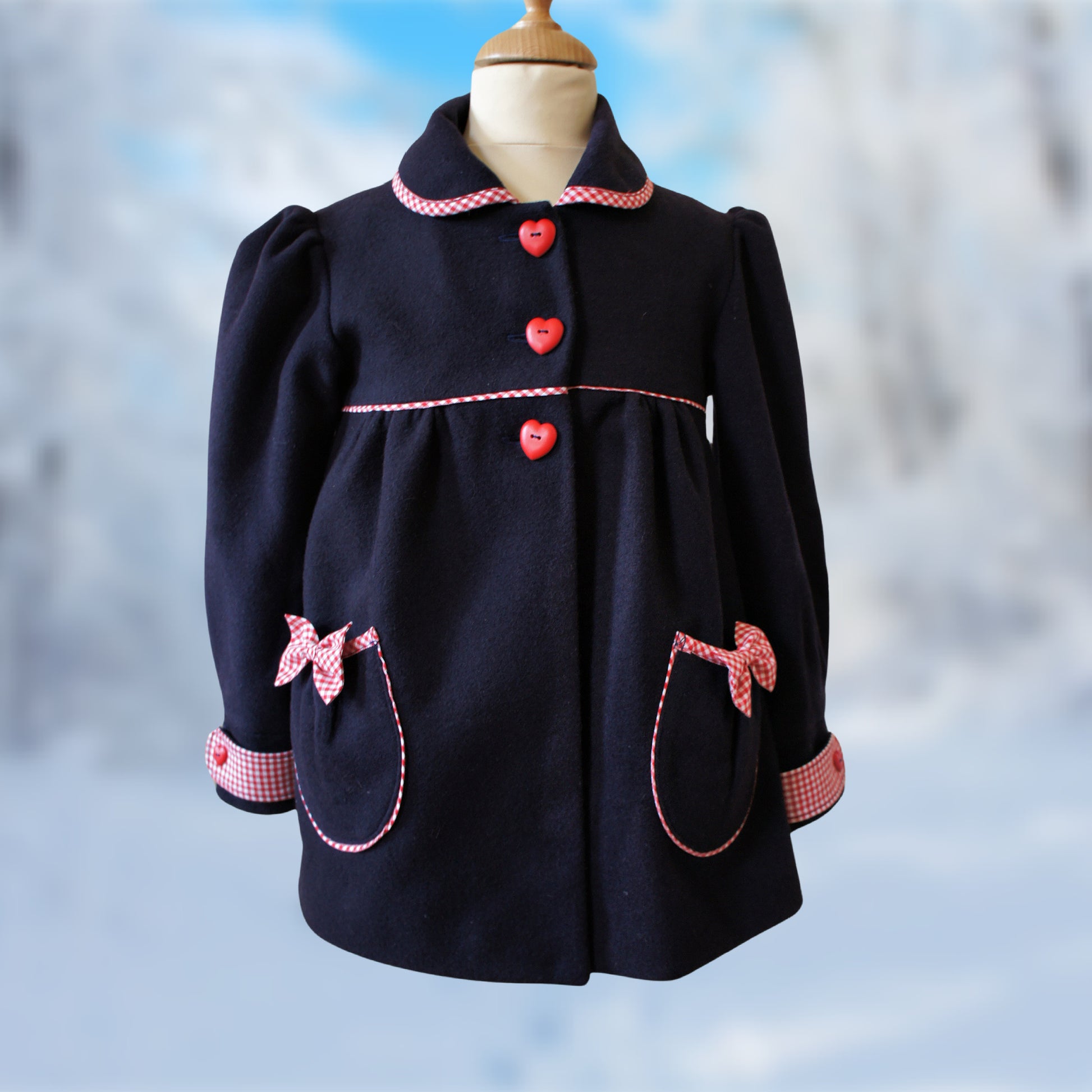 Charlotte girls coat, pdf sewing pattern by Frocks & Frolics. In boiled dark blue wool and red and white gingham trim. Long puff sleeves with cuffs and tabs. Featuring a yoke and rounded collar.