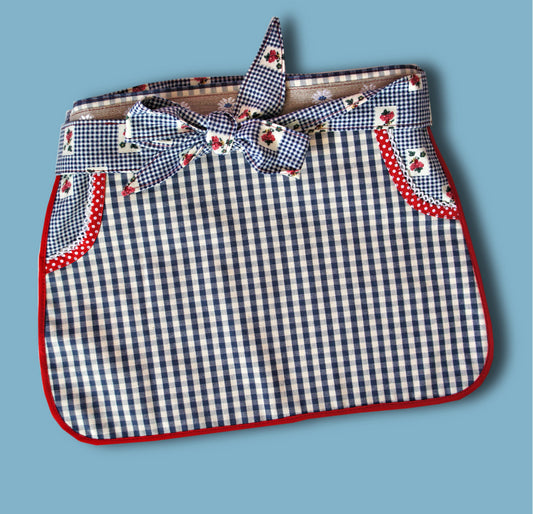 Half apron Pdf sewing pattern by Frocks & Frolics. Fully lined, cute tie backs, free video sew-a-long. In gingham white and blue cotton with red trim bias binding and pockets.