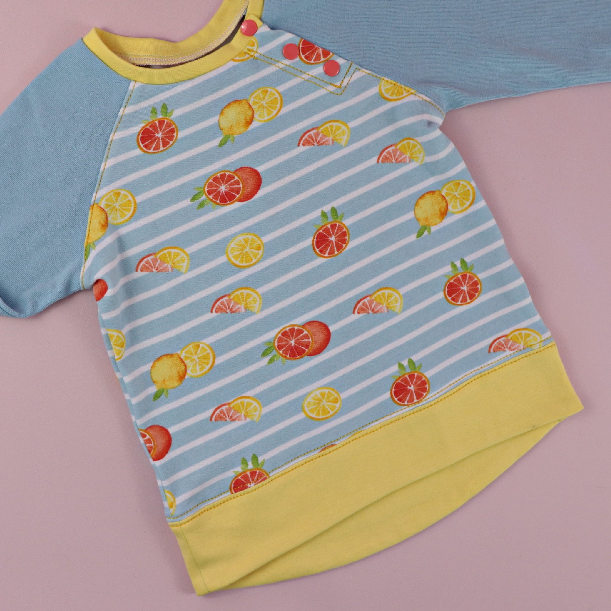 Jelly Bean Sweater, pdf sewing pattern by Frocks & Frolics. Raglan jumper with optional KamSnap opening in the raglan sleeve seam. High low hem trim and cuffs in contrast four way stretch interlock fabric. Includes a free video tutorial.