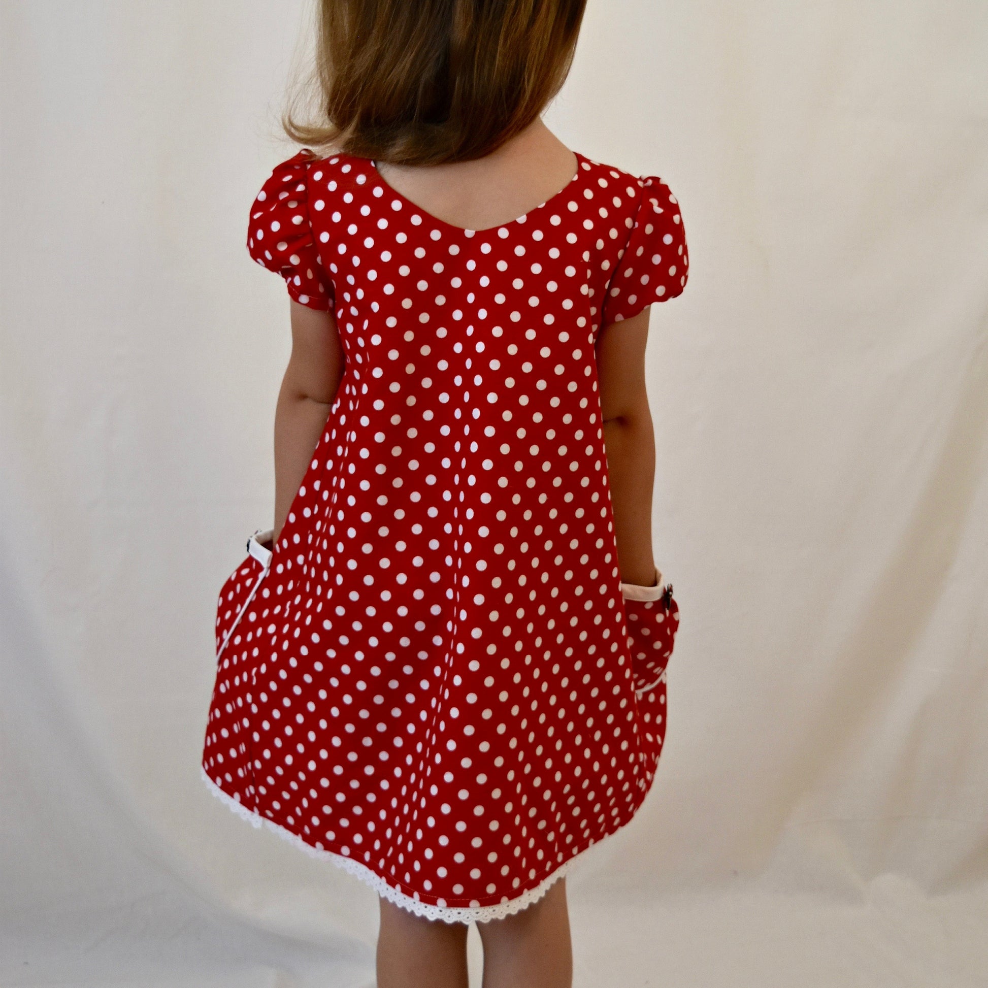 Millie dress pdf sewing pattern by Frocks & Frolics. Empire line bodice and slightly gathered skirt. Puff sleeves with elastication. Patch pockets with piping. Bodice has a cute lace trim. The fabric is white polka dots on a red cotton.