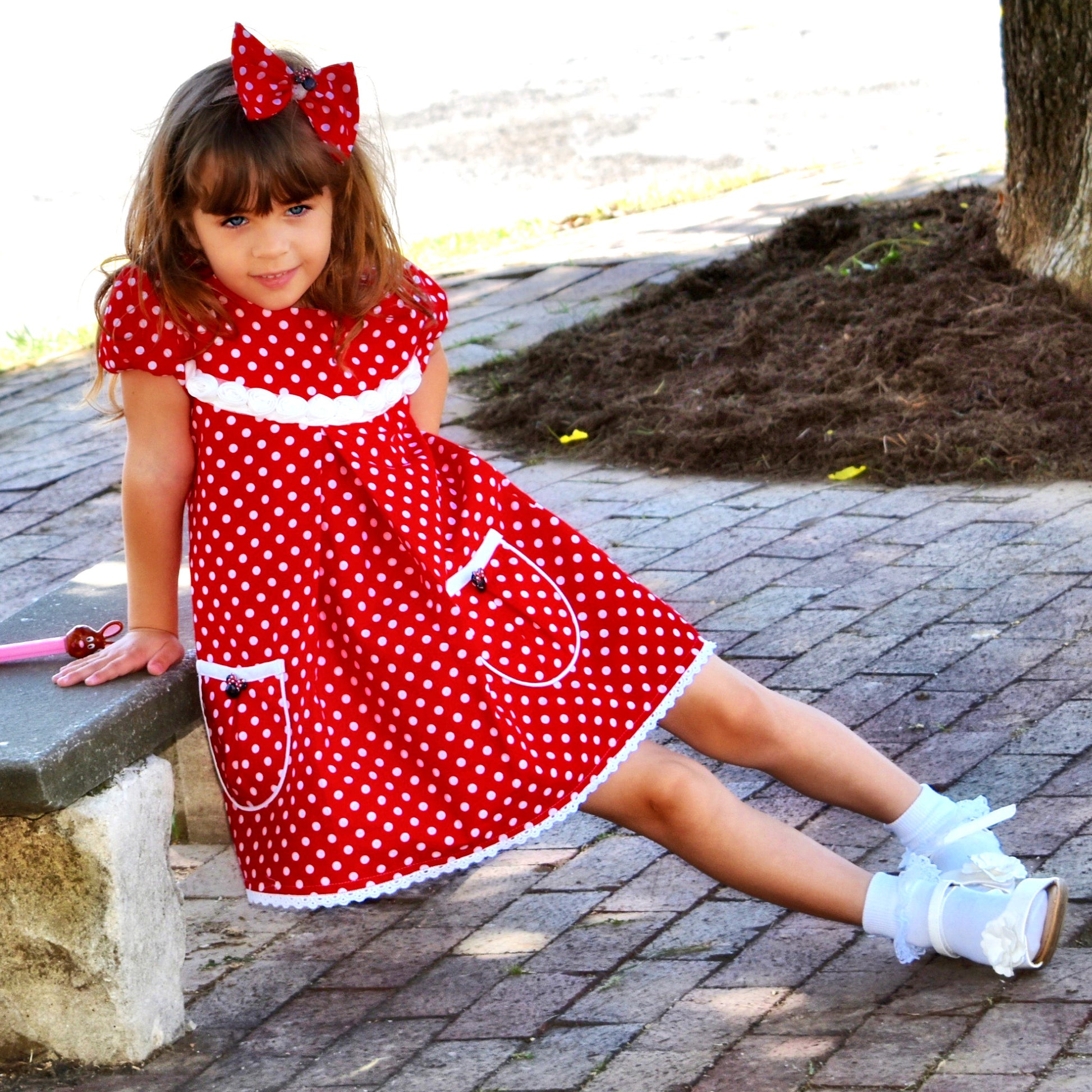 Millie dress pdf sewing pattern by Frocks & Frolics. Empire line bodice and slightly gathered skirt. Puff sleeves with elastication. Patch pockets with piping. Bodice has a cute lace trim. The fabric is white polka dots on a red cotton.