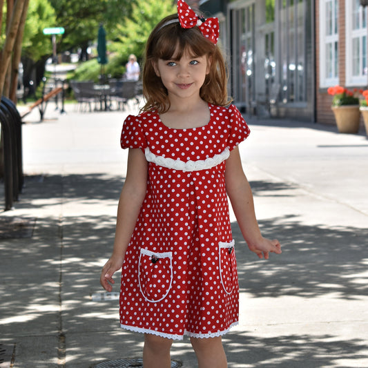 Millie dress pdf sewing pattern by Frocks & Frolics. Empire line bodice and slightly gathered skirt. Puff sleeves with elastication. Patch pockets with piping. Bodice has a cute lace trim. The fabric is white polka dots on a red cotton.