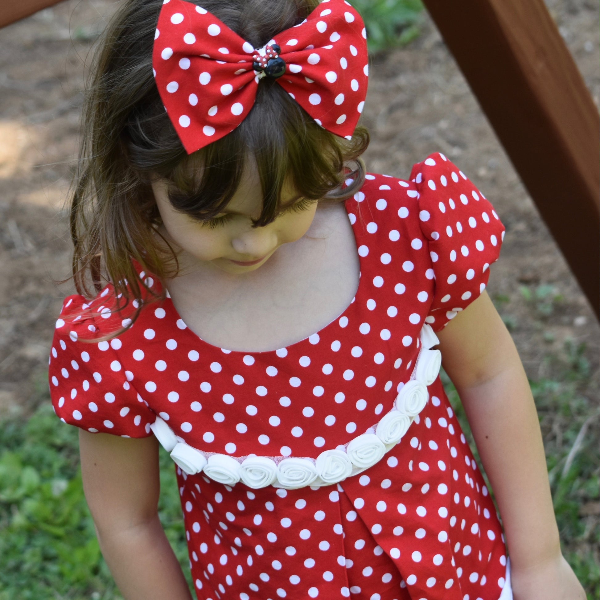 Millie dress pdf sewing pattern by Frocks & Frolics. Empire line bodice and slightly gathered skirt. Puff sleeves with elastication. Patch pockets with piping. Bodice has a cute lace trim. The fabric is white polka dots on a red cotton.