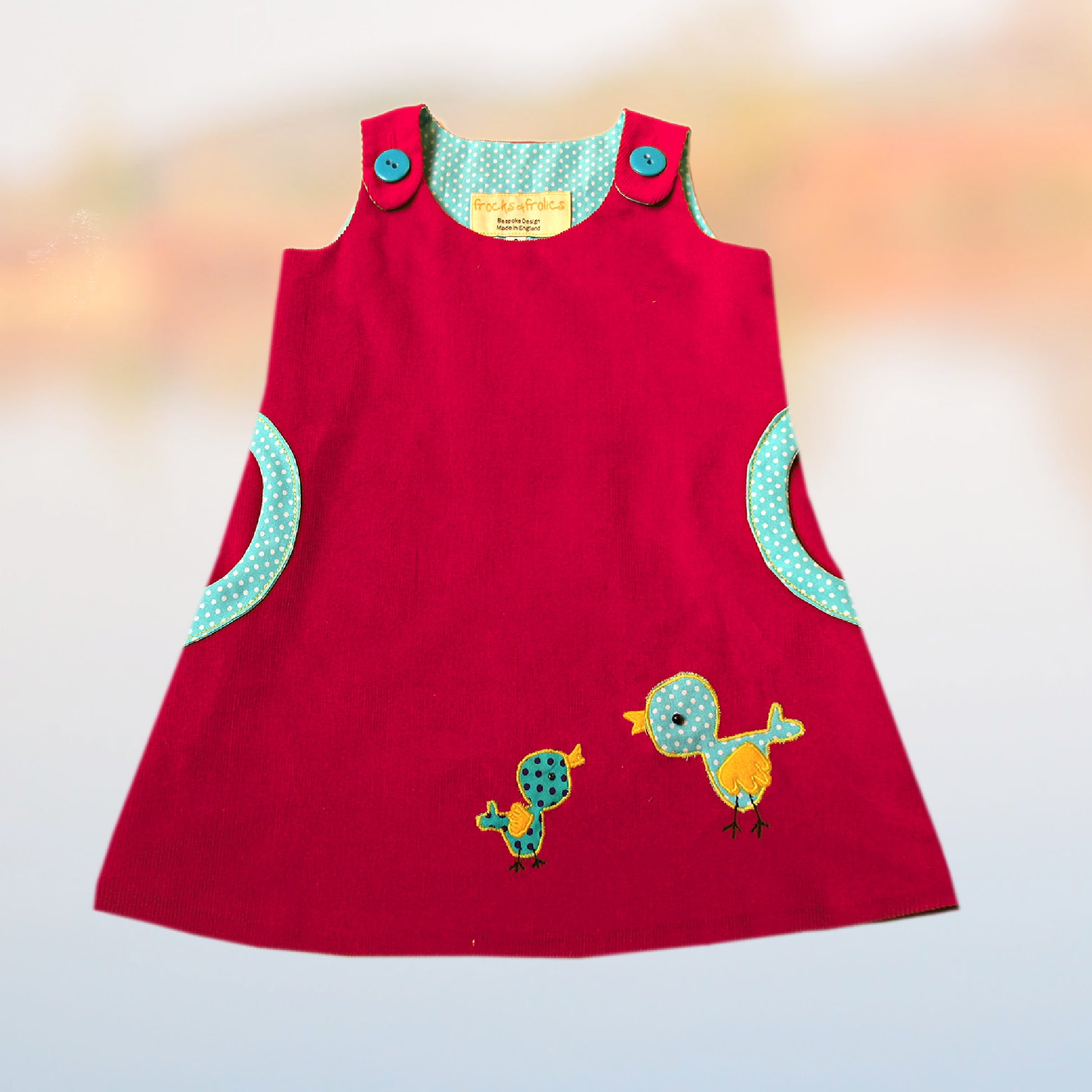 Mimi apron dress pdf sewing pattern. For girls age 1-12. Fully lined with side pockets and cute applique. In red cord and polka dot accent. Close up of the lining and the button closure.