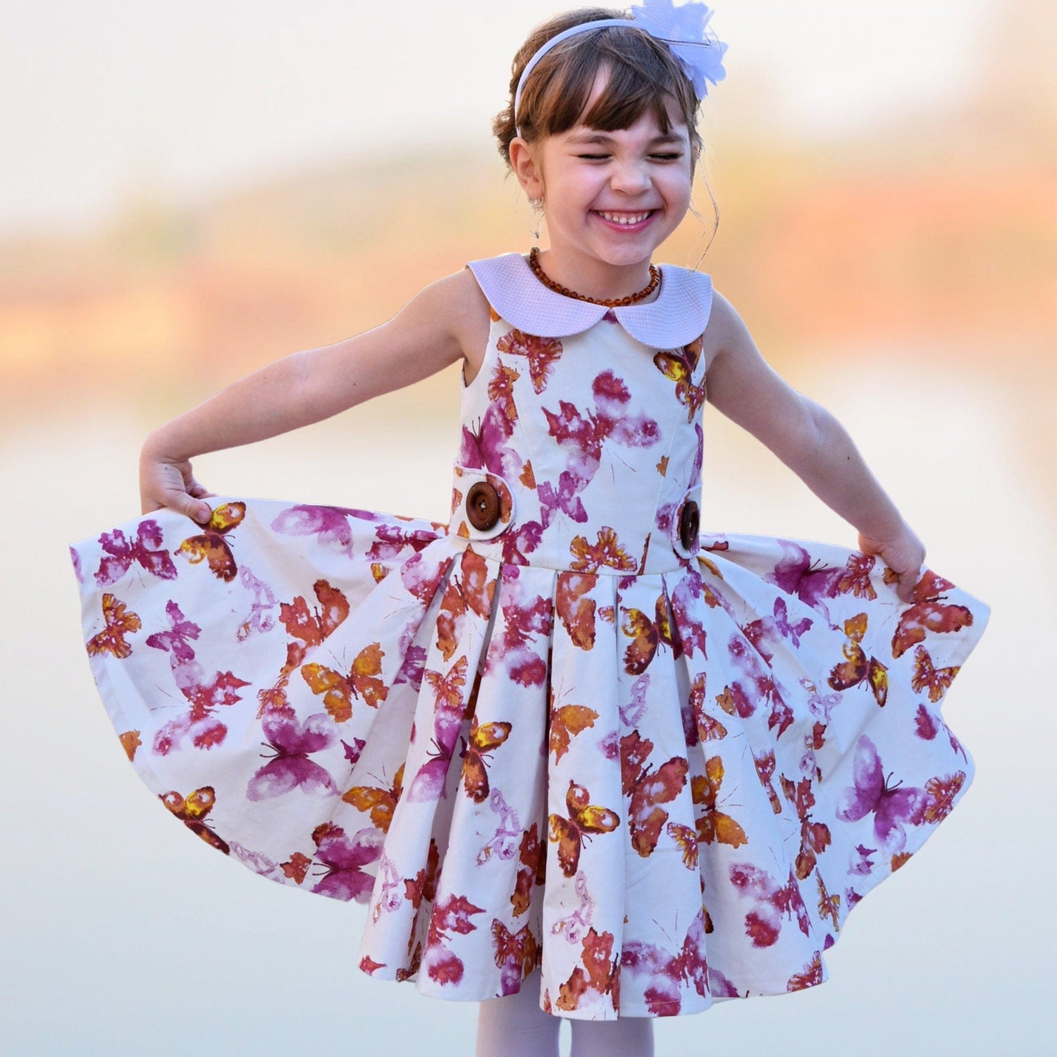 Vivienne dress for girls by Frocks & Frolics. Princess seam bodice, a sleeveless dress printed denim. Peter Pan collar with lower cut back. Pleated skirt. Large feature tabs with oversized button. Concealed zipper.