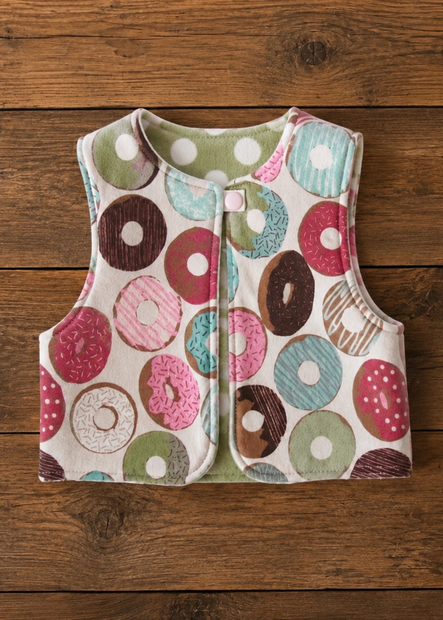 Flat lay of the colorful donut print reversible vest sewing pattern with polka dot lining and snap closure