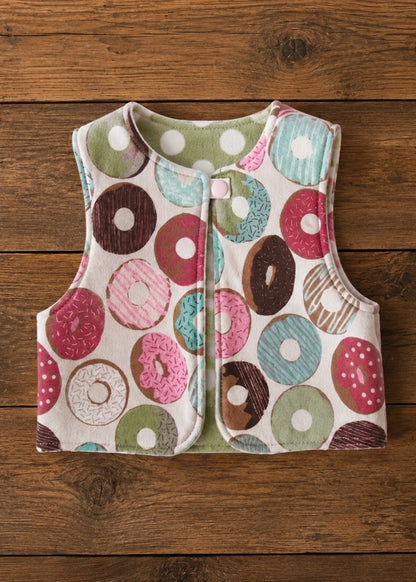 Flat lay of the colorful donut print reversible vest sewing pattern with polka dot lining and snap closure