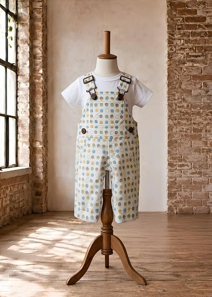Close-up view of handmade overalls featuring a colorful polka dot fabric, a pink gingham inner lining, and brass hardware including an overall clasp and engraved side button.