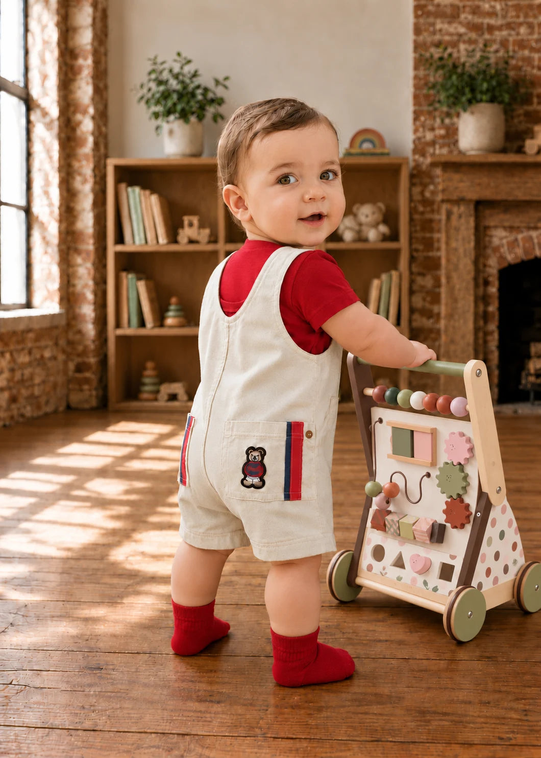 Bobby Dazzler Dungarees sewing pattern – baby in cream dungarees and red tee with a walker, back view