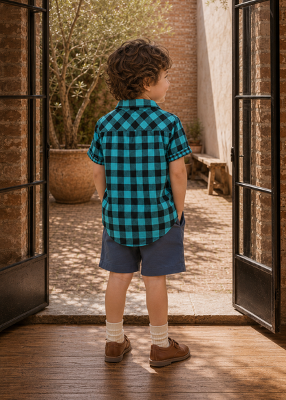 Back view of a boy in a teal and black plaid Cool Shirt and navy shorts standing by the doorway