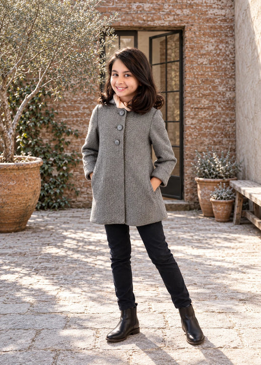 Dakota Pea Coat sewing pattern – girl in a short grey wool A-line coat with black jeans, front view in a sunny courtyard