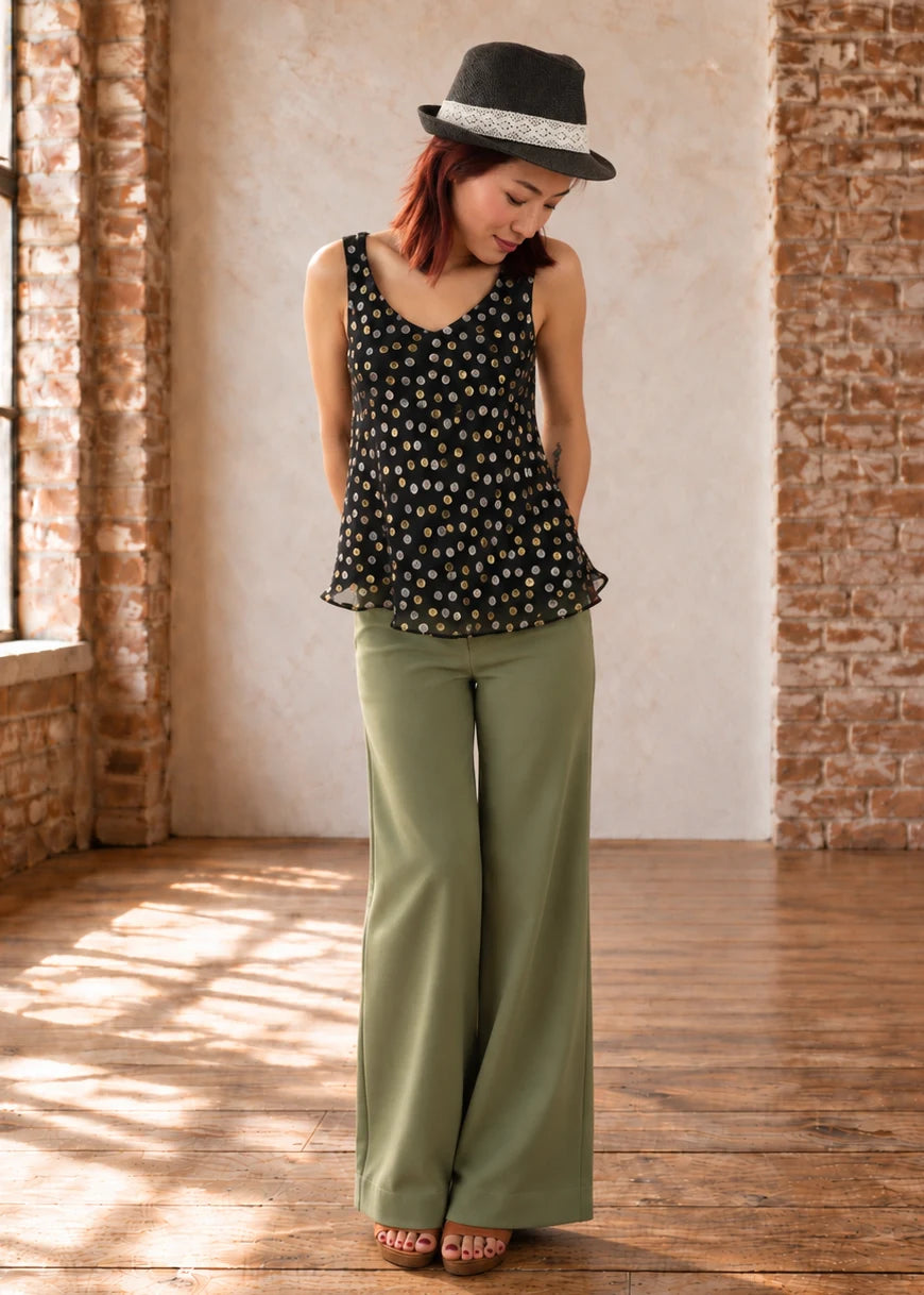 Devon Pants sewing pattern – sage green linen pants with a black floral top and fedora, front view indoors
