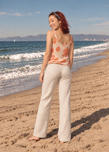 Devon Pants sewing pattern – back view of beige linen straight-leg pants with an orange print camisole on the beach