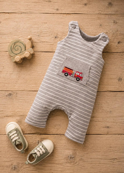 A baby romper laid flat on a wooden surface, featuring thin gray and white stripes and an embroidered red fire truck on the chest pocket. A wooden snail toy and a pair of baby shoes are styled around it.