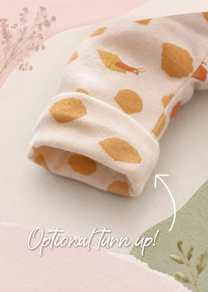 A close-up of a baby sleeve or cuff made from soft cream fabric with a mustard yellow and orange leaf print, shown on a styled pastel background with the text 'Optional turn up!' and a curved arrow pointing to the cuff.
