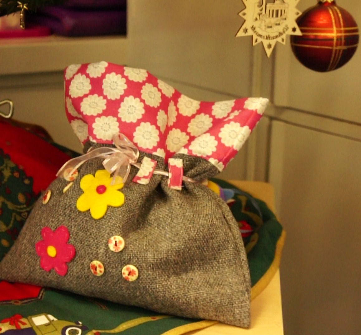 Decorative gift bag with floral design and pink flower hat on a colorful surface.