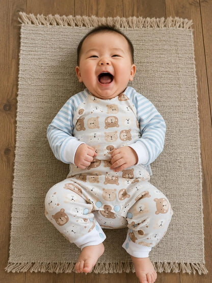 A baby lying on a woven beige rug, wearing a light blue and white striped long-sleeve top with a bib-style front panel covered in brown teddy bear prints, paired with matching printed pants.
