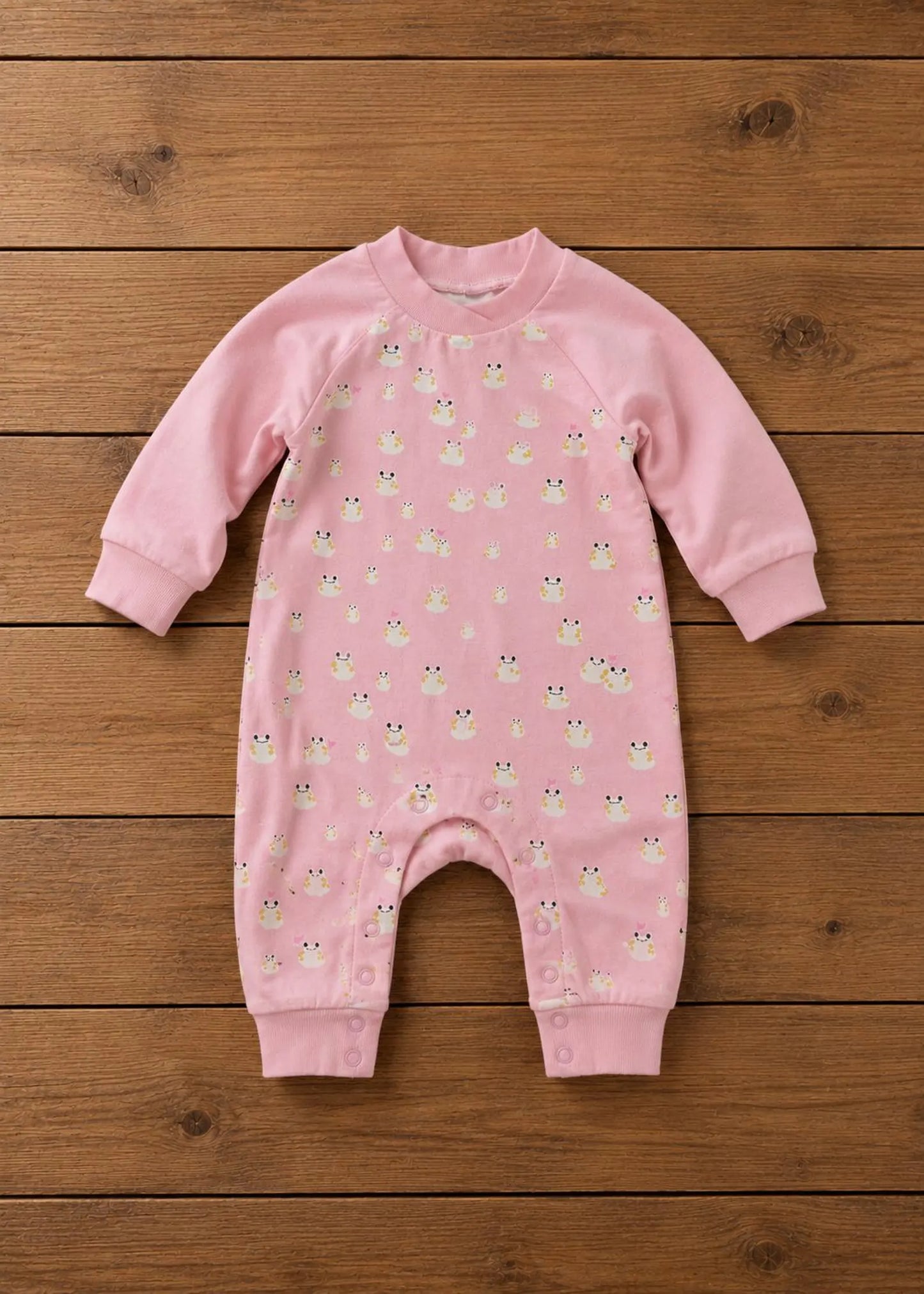 A pink long-sleeve baby jumpsuit with a small owl pattern, laid flat on a wooden plank background.