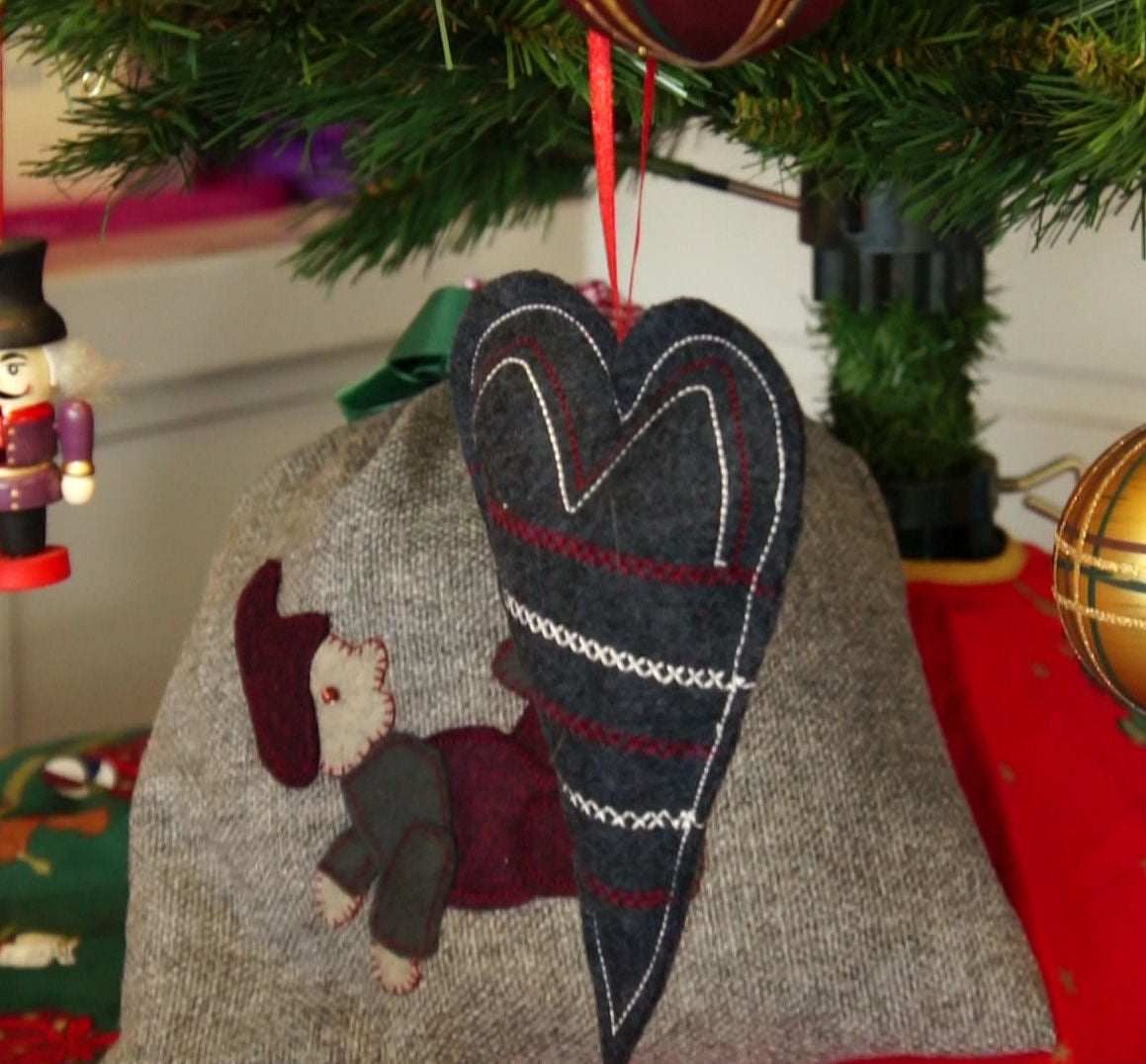 Heart-shaped ornament with teddy bear design hanging on a Christmas tree.