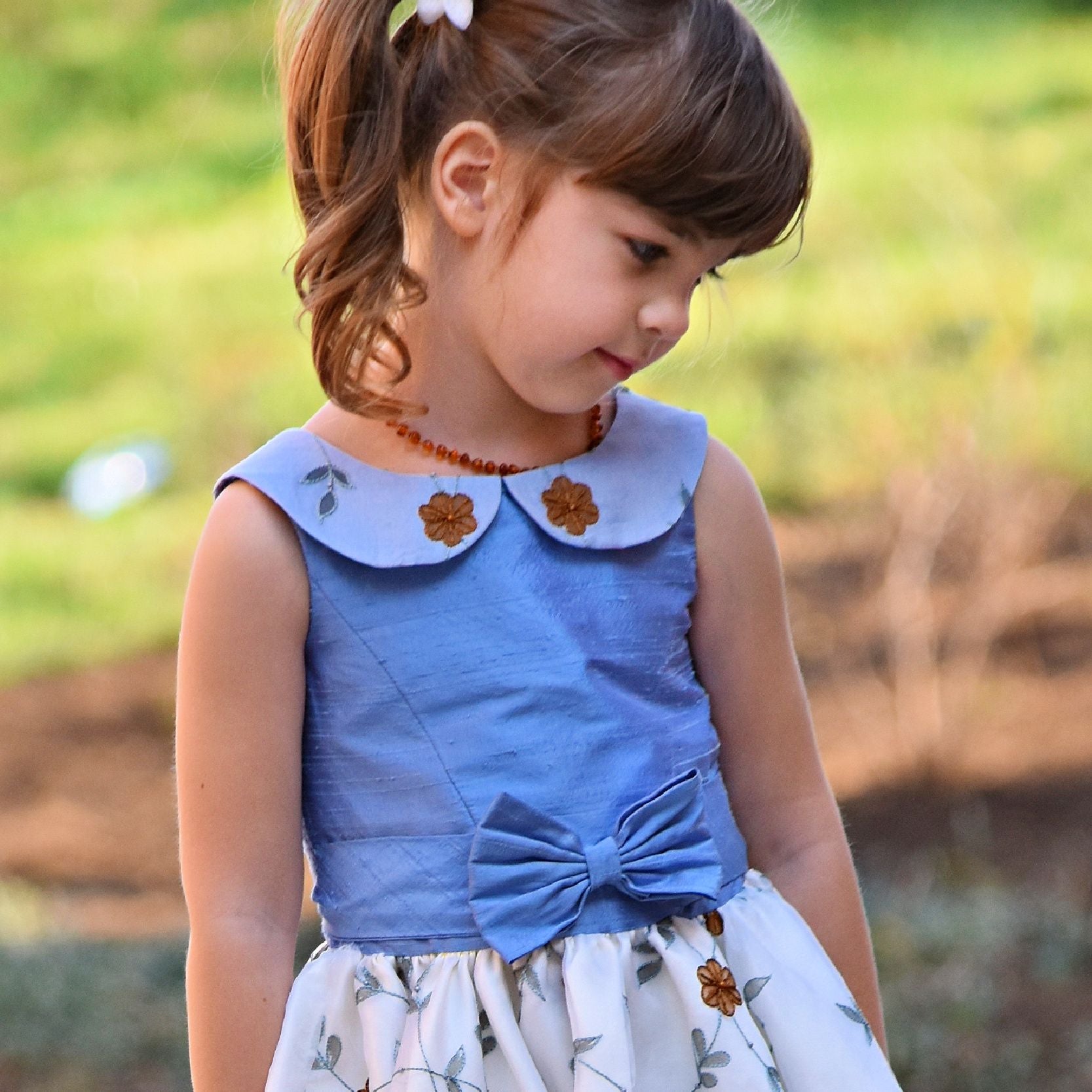 Vivienne dress for girls by Frocks & Frolics. Princess seam bodice, a sleeveless dress with dupion silk bodice and embroidered chiffon circle skirt. The silk Peter Pan collar is also covered in embroidered chiffon. Here the dress has a feature tie and front bow. Concealed zipper. 