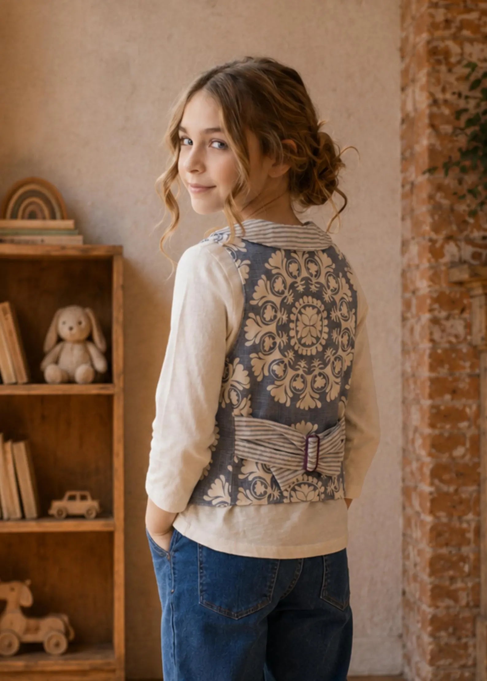 Girl looking over her shoulder wearing a blue damask pattern waistcoat with a striped lapel collar and matching back strap.