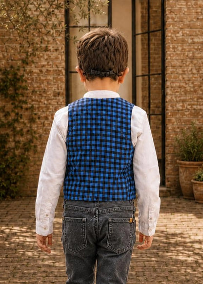 Young boy wearing glasses, a blue and black check Brooklyn waistcoat, white collarless shirt, and black jeans.