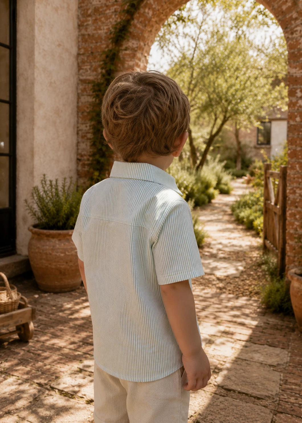 Back view of a preteen boy in a white t-shirt and football team-print Oscar Shorts standing barefoot on a wooden dock