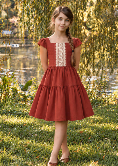Isabella Dress PDF sewing pattern. Girl by a willow tree wearing a red tiered vintage-style dress with cap sleeves, square neckline and lace front panel.