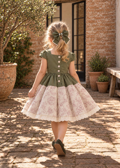 Isabella Dress PDF sewing pattern. Back view of a little girl with a hair bow in a green bodice dress with button back and gathered pink floral skirt with lace hem.