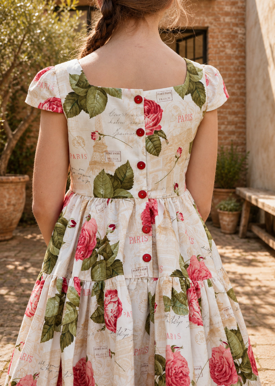 Isabella Dress PDF sewing pattern. Close-up back view of the rose print dress showing the red button back closure, cap sleeves and tiered skirt.