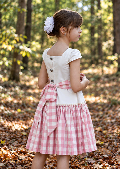 Isabella Dress PDF sewing pattern. Christmas version: back view of a girl in a white bodice dress with button back, pink gingham tiered skirt and large gingham sash bow.