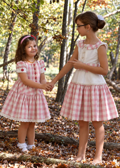 Isabella Dress PDF sewing pattern. Christmas version: two sisters holding hands in the woods wearing matching pink gingham Isabella dresses in different sizes.