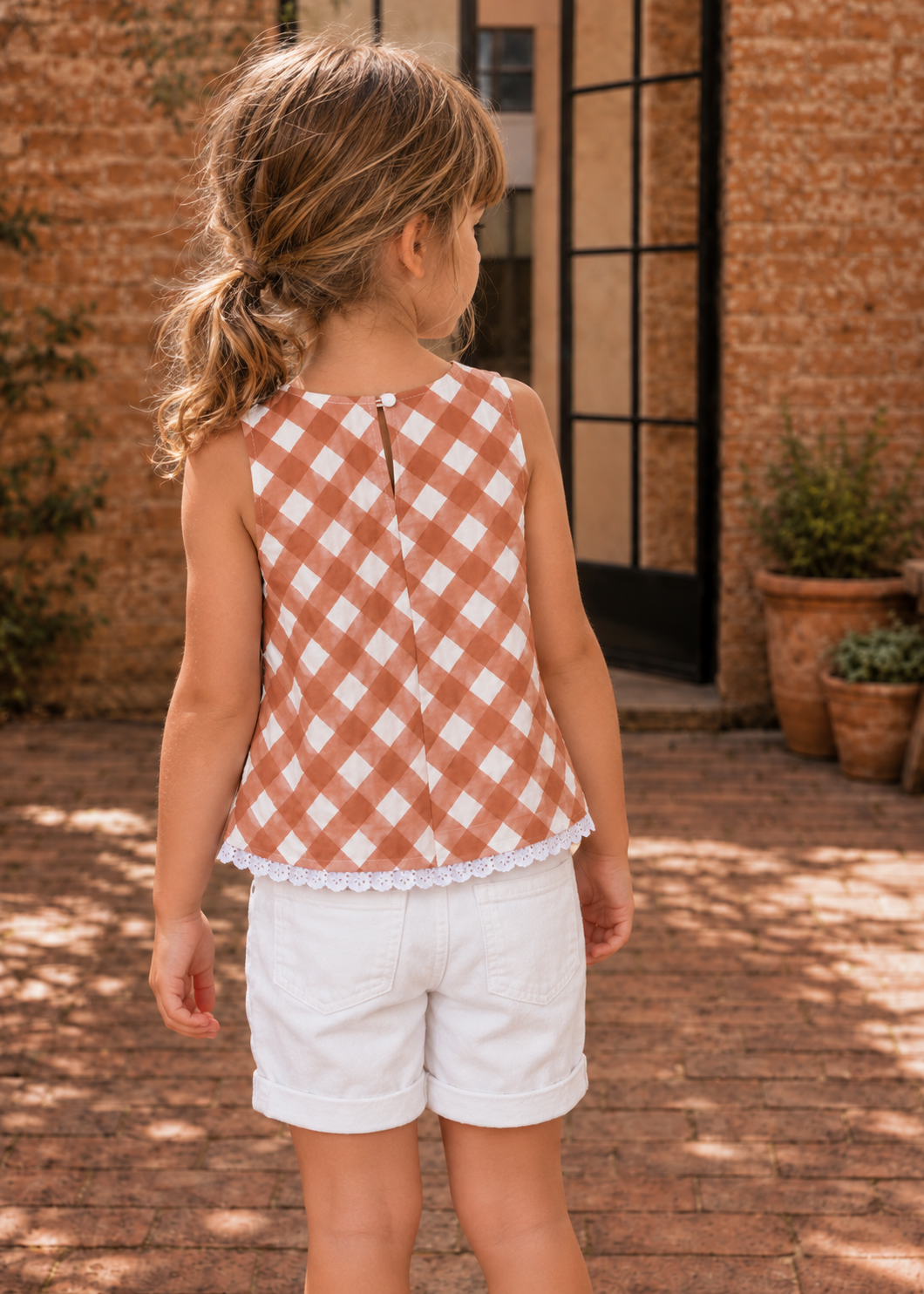 Back view of a terracotta check sleeveless top with button back and lace hem, made with the Lily blouse PDF sewing pattern by Frocks & Frolics, worn with white shorts