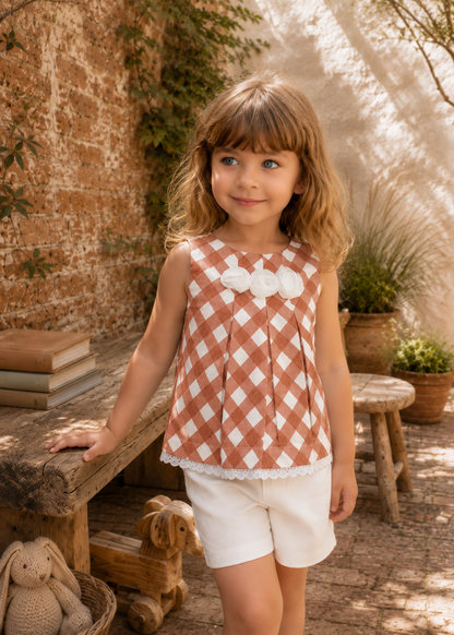 Smiling girl in a terracotta check sleeveless top with front pleats and white shorts, made with the Lily blouse PDF sewing pattern by Frocks & Frolics
