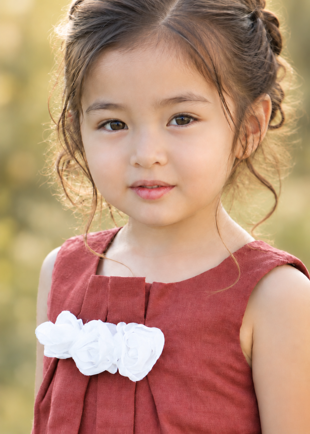 Close-up of a girl wearing a rust red sleeveless top with front pleats and a white fabric flower detail, sewn with the Lily blouse PDF sewing pattern by Frocks & Frolics
