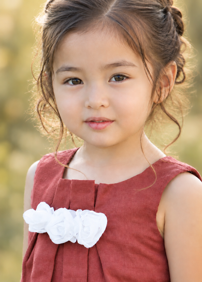 Close-up of a girl wearing a rust red sleeveless top with front pleats and a white fabric flower detail, sewn with the Lily blouse PDF sewing pattern by Frocks & Frolics