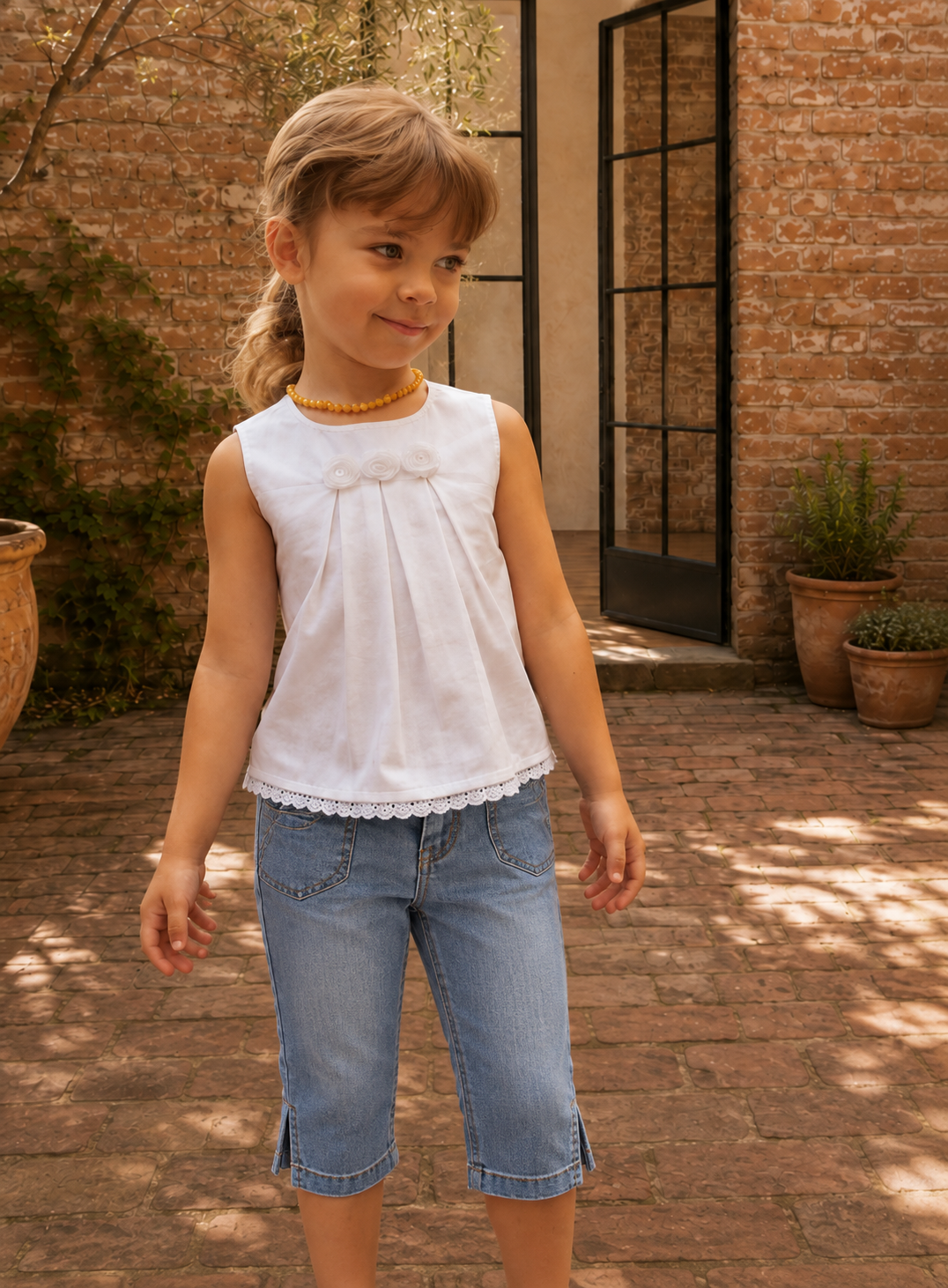Girl wearing a white sleeveless top with front pleats and lace hem, made with the Lily blouse PDF sewing pattern by Frocks & Frolics, styled with denim jeans