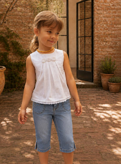 Girl wearing a white sleeveless top with front pleats and lace hem, made with the Lily blouse PDF sewing pattern by Frocks & Frolics, styled with denim jeans