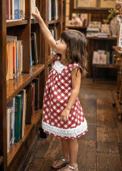 Girl reaching for a book on a shelf, wearing a terracotta check A-line dress with lace hem made with the Lily dress PDF sewing pattern by Frocks & Frolics
