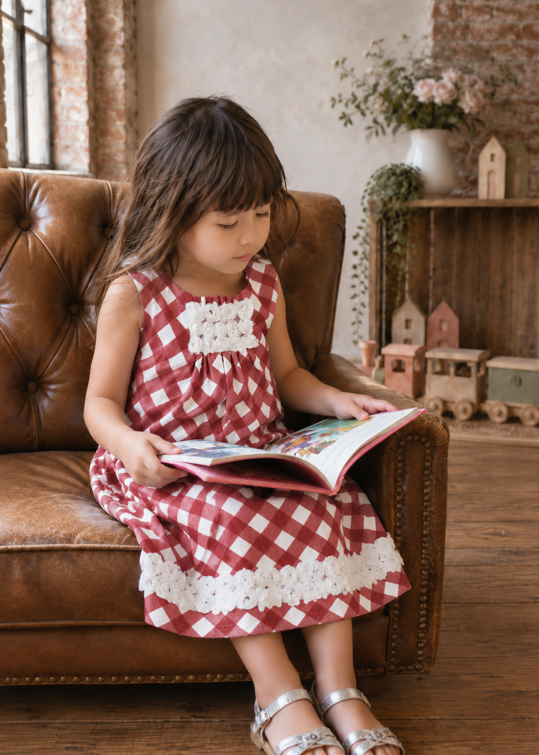 Girl sitting on a leather sofa reading, wearing a terracotta check dress with lace hem made with the Lily dress PDF sewing pattern by Frocks & Frolics