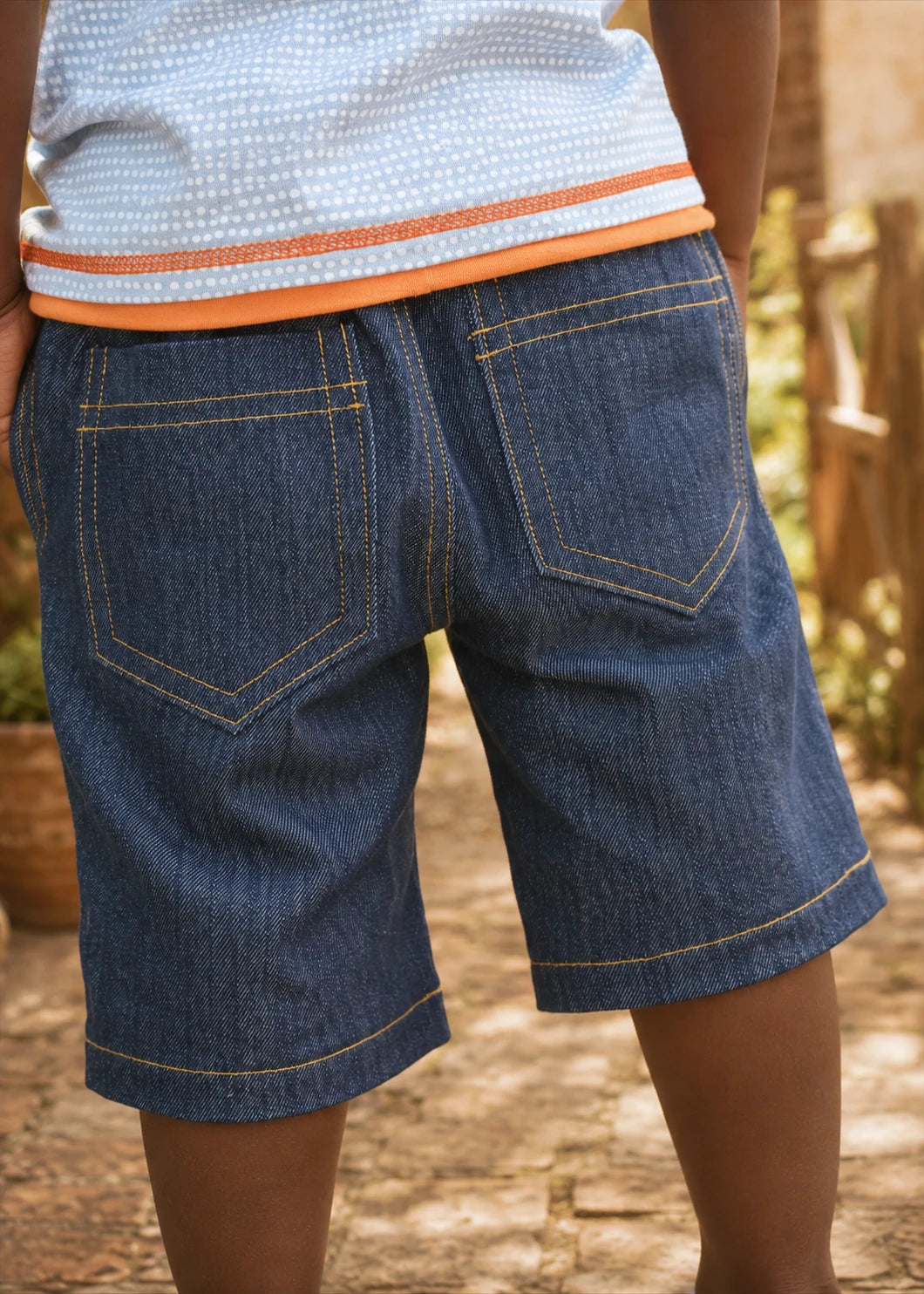 Close-up side view of the Oscar Shorts denim fabric showing the angled side pocket, back patch pocket with tab, and contrast topstitching