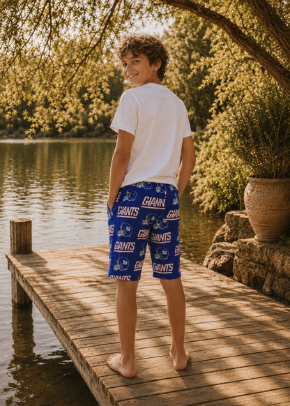 Back view of a preteen boy in a white t-shirt and football team-print Oscar Shorts standing barefoot on a wooden dock